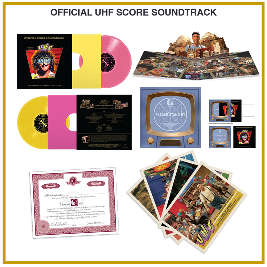 Official UHF Score Soundtrack vinyl set displayed on a white background with a gold border. The set includes a black LP with a pink inner sleeve, a yellow LP with a pink inner sleeve, a large illustrated book or booklet, several small printed cards or inserts, a blue console-style case, and a certificate.
